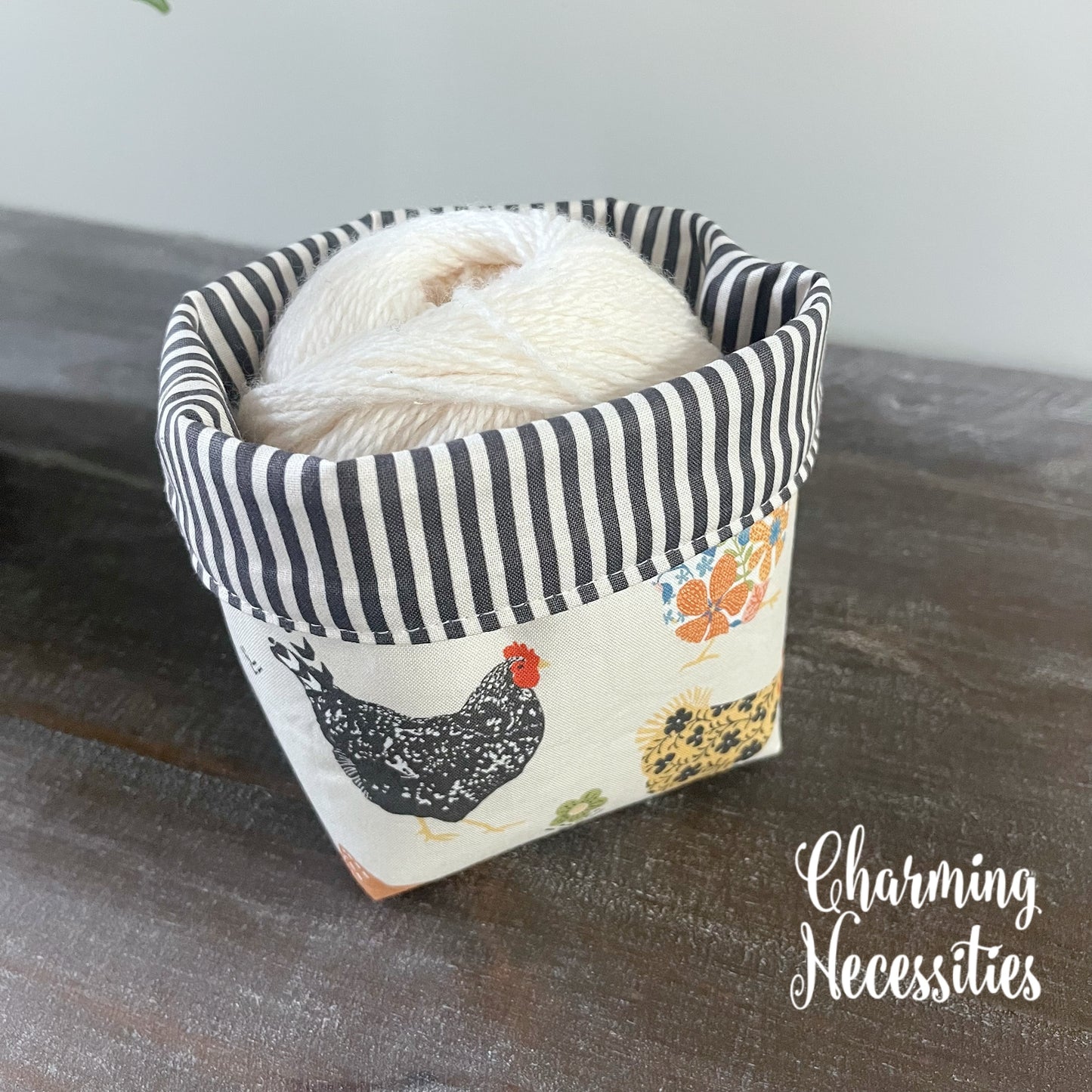 Fabric yarn bowl with striped interior and chicken design on a wooden surface, containing yarn.