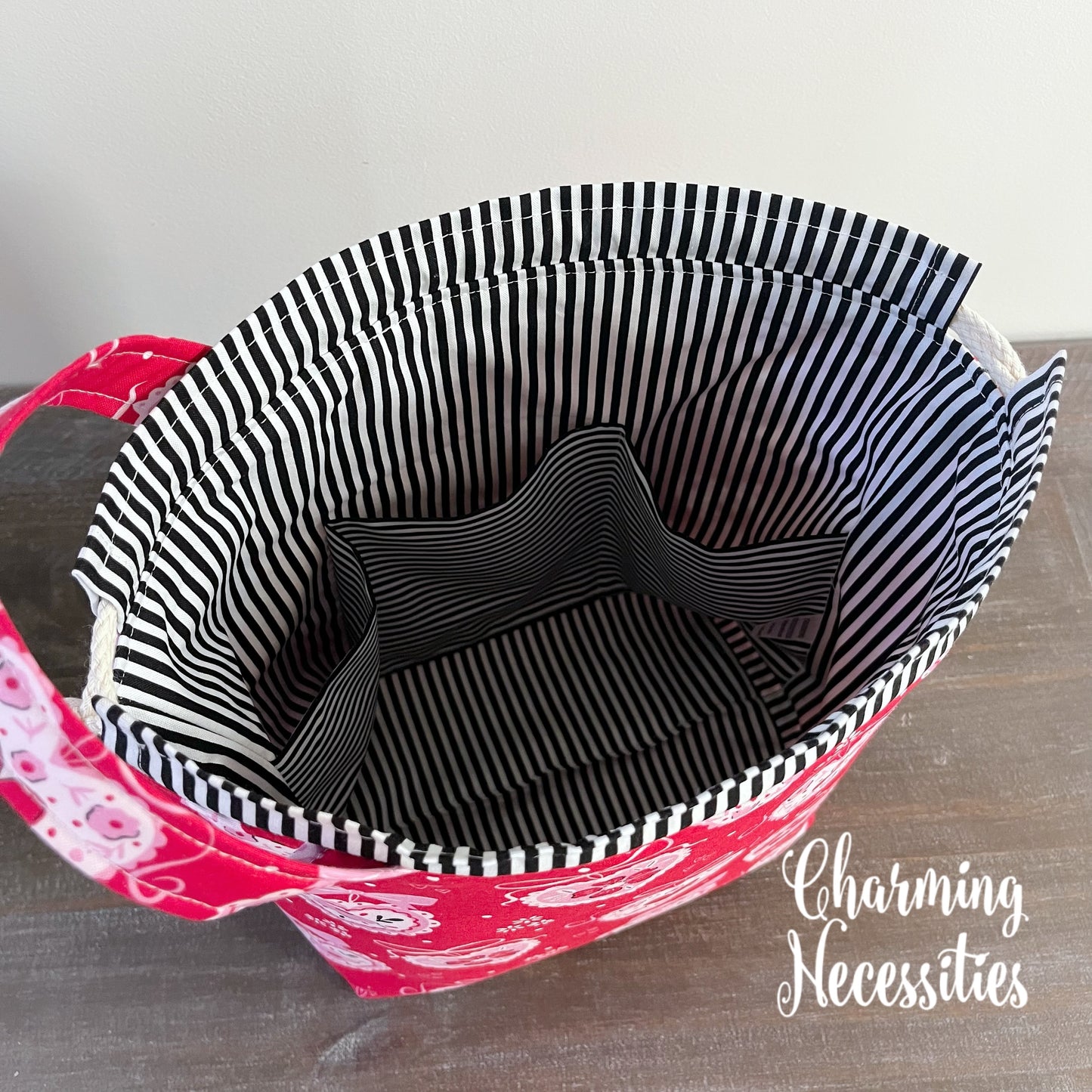 Red bag with black and white striped lining on a wooden surface, featuring 'Charming Necessities' branding.