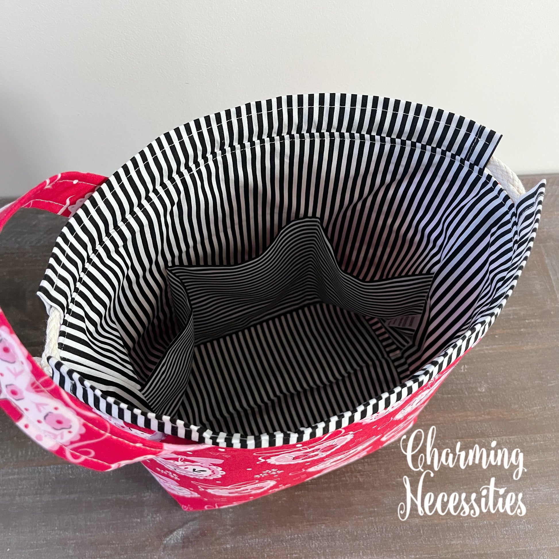 Red bag with black and white striped lining on a wooden surface, featuring 'Charming Necessities' branding.