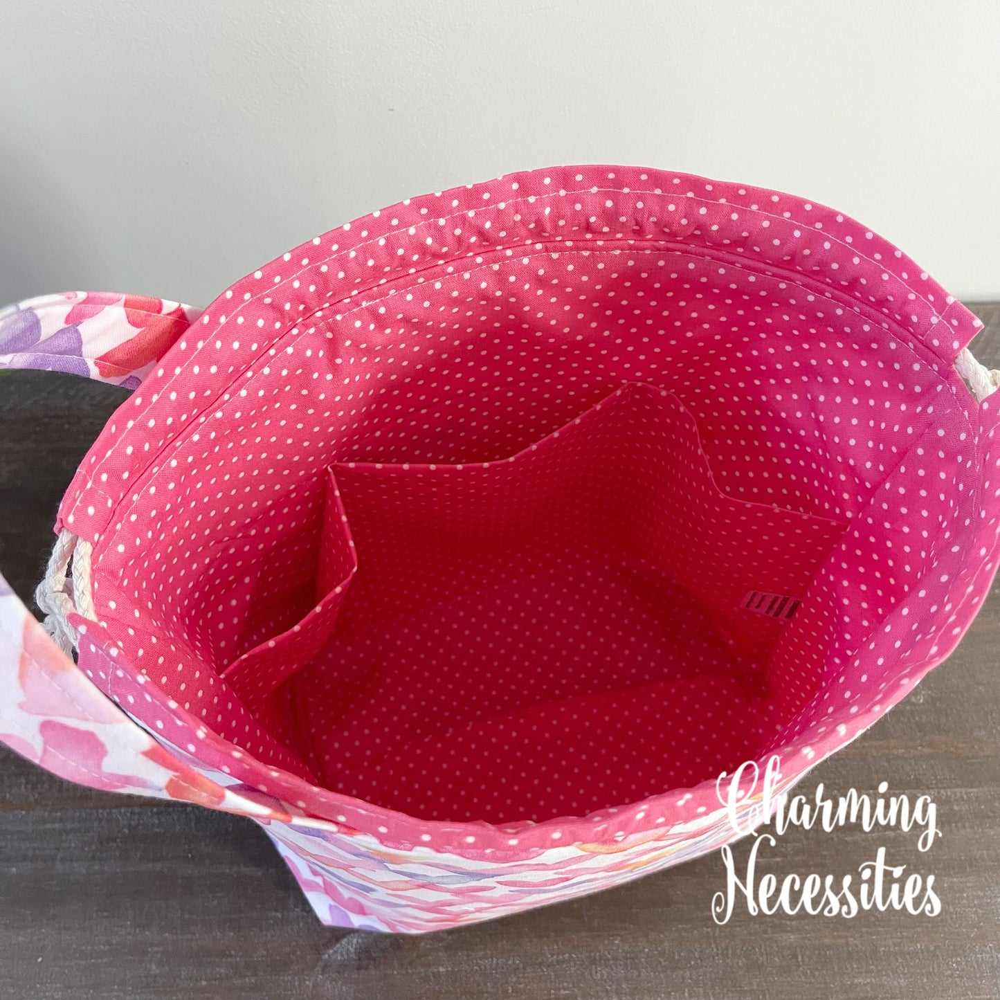 Pink polka dot fabric bag with hearts pattern on a gray background, featuring 'Charming Necessities' branding.