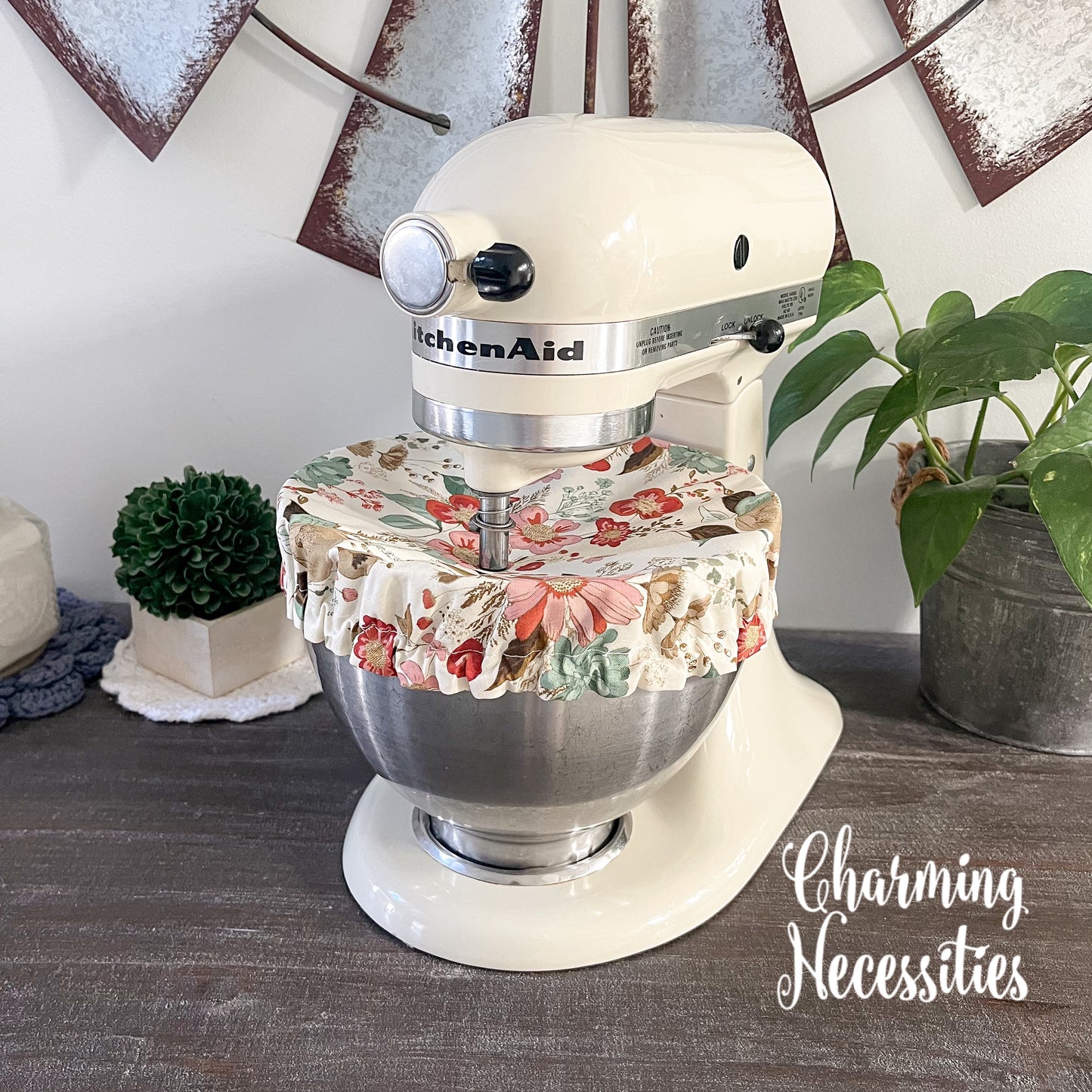 KitchenAid mixer with a floral cover on a wooden surface, surrounded by decorative items.