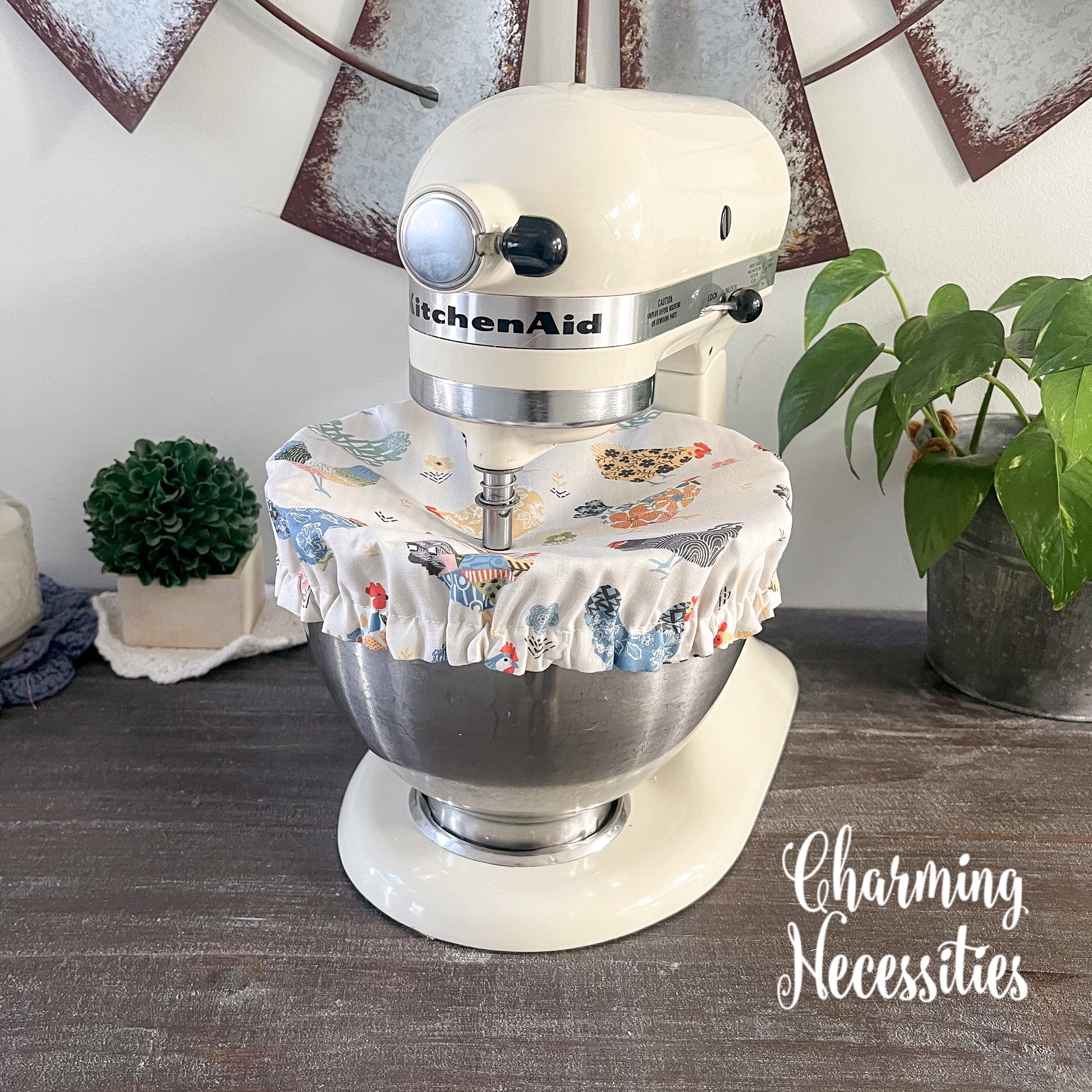 KitchenAid mixer with a chicken print bowl cover on a wooden surface, surrounded by decorative elements