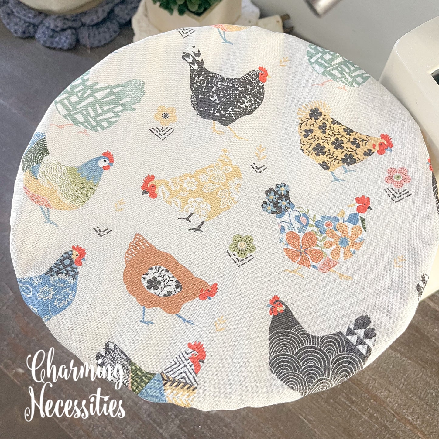 Bowl cover with chicken pattern on a surface, branded 'Charming Necessities'.