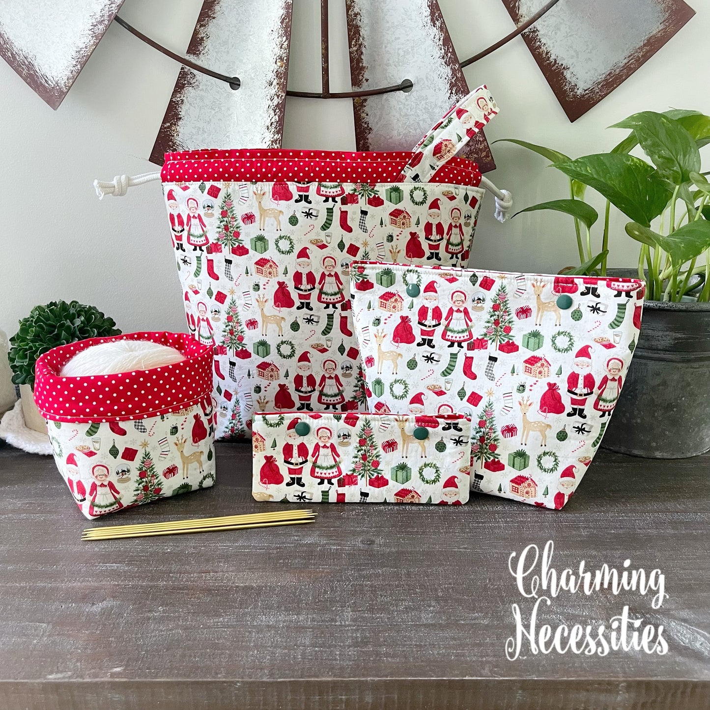 Set of fabric knitting project bags with Christmas patterns on a wooden surface, featuring the brand 'Charming Necessities'.