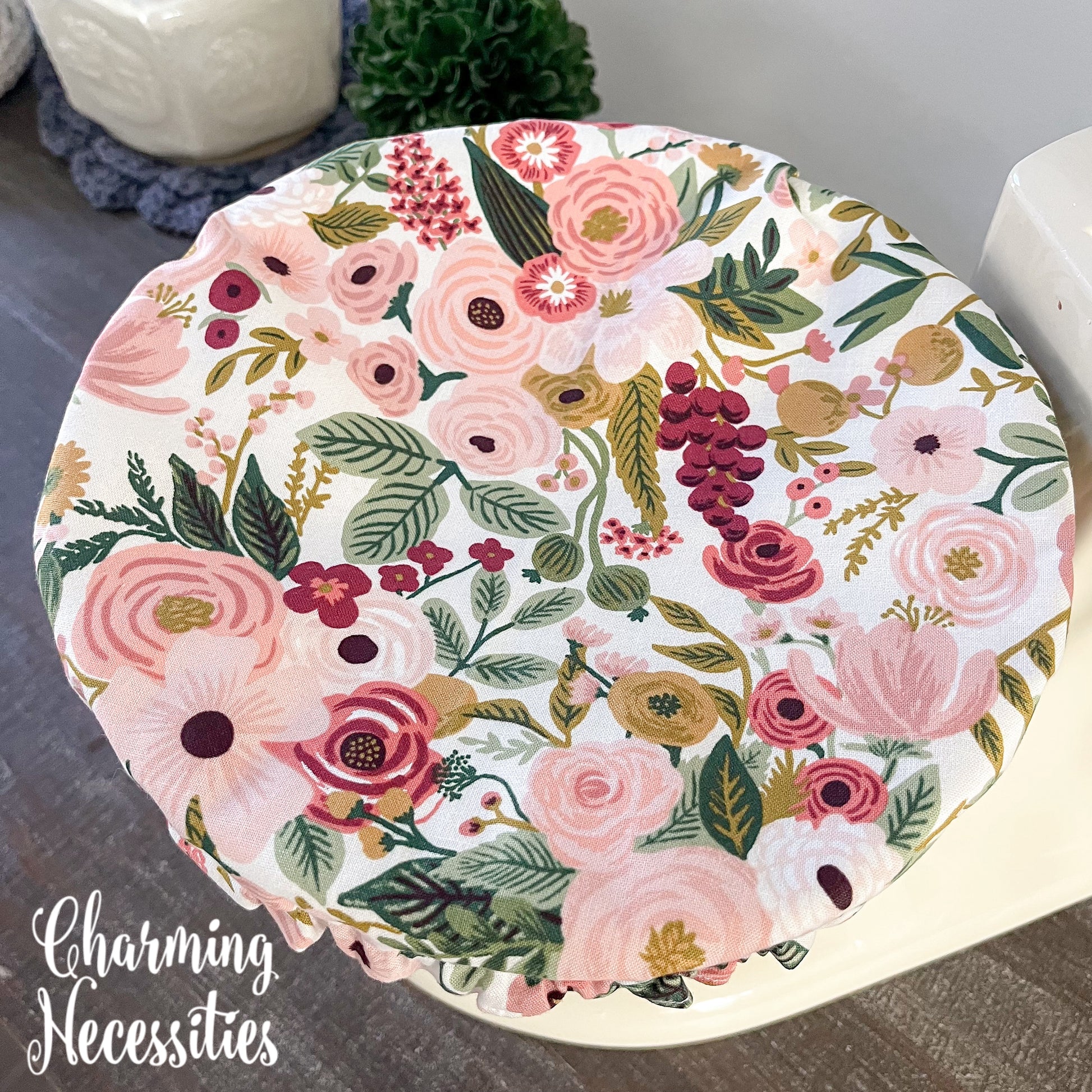 Floral-patterned bowl cover with 'Charming Necessities' branding on a wooden surface.