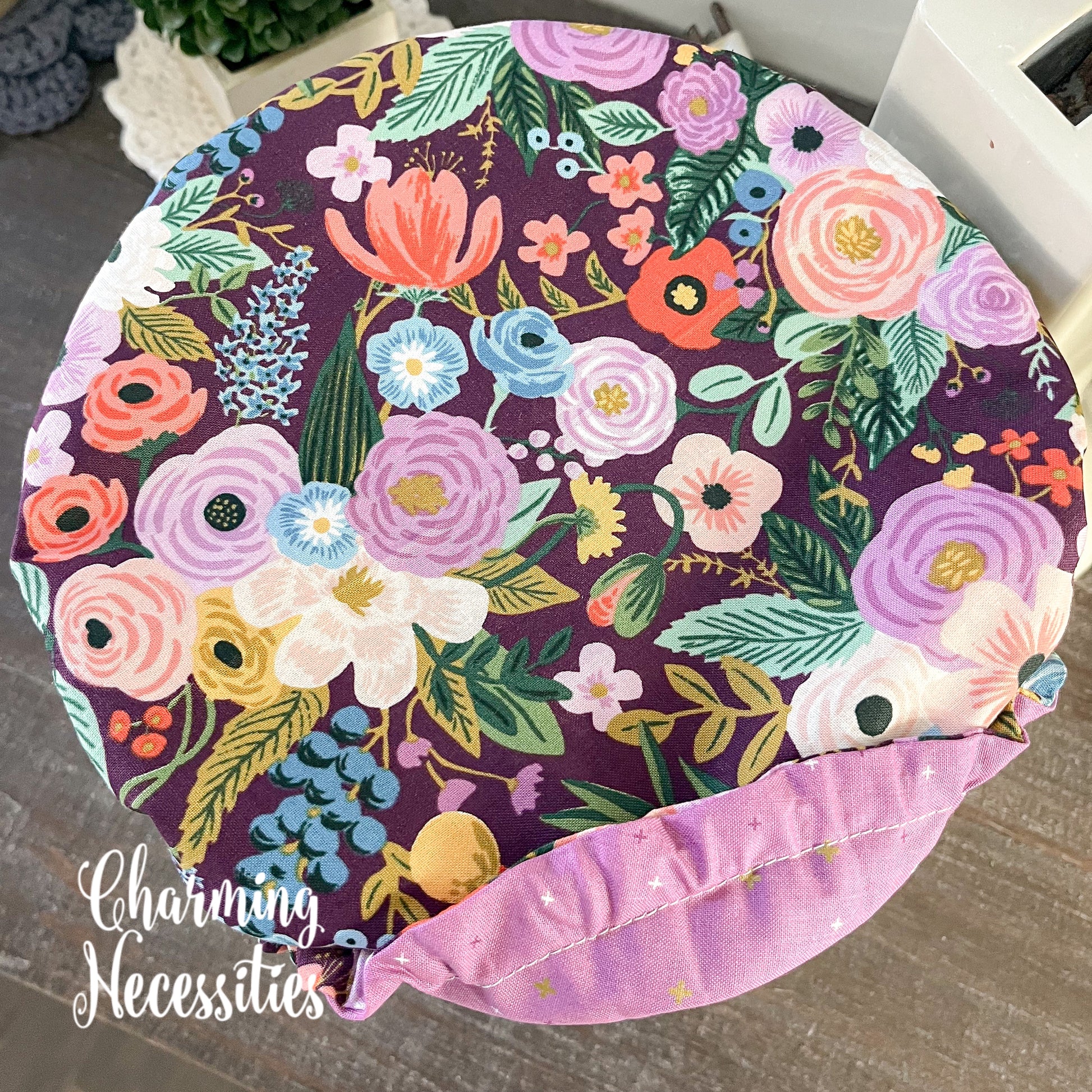 Floral-patterned bowl cover with colorful flowers on a dark purple background, branded 'Charming Necessities'.