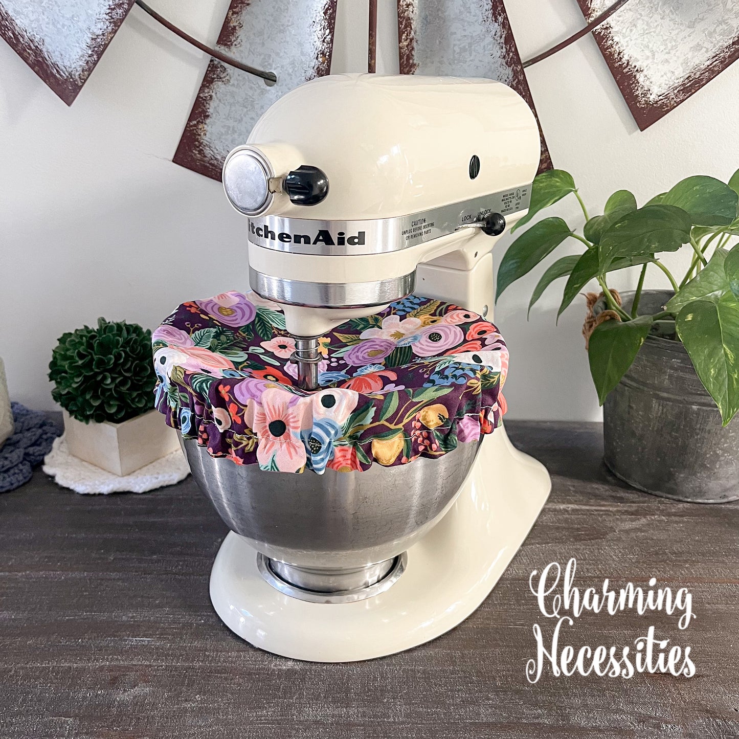KitchenAid mixer with a burgandy floral cover on a wooden surface, surrounded by decorative elements.