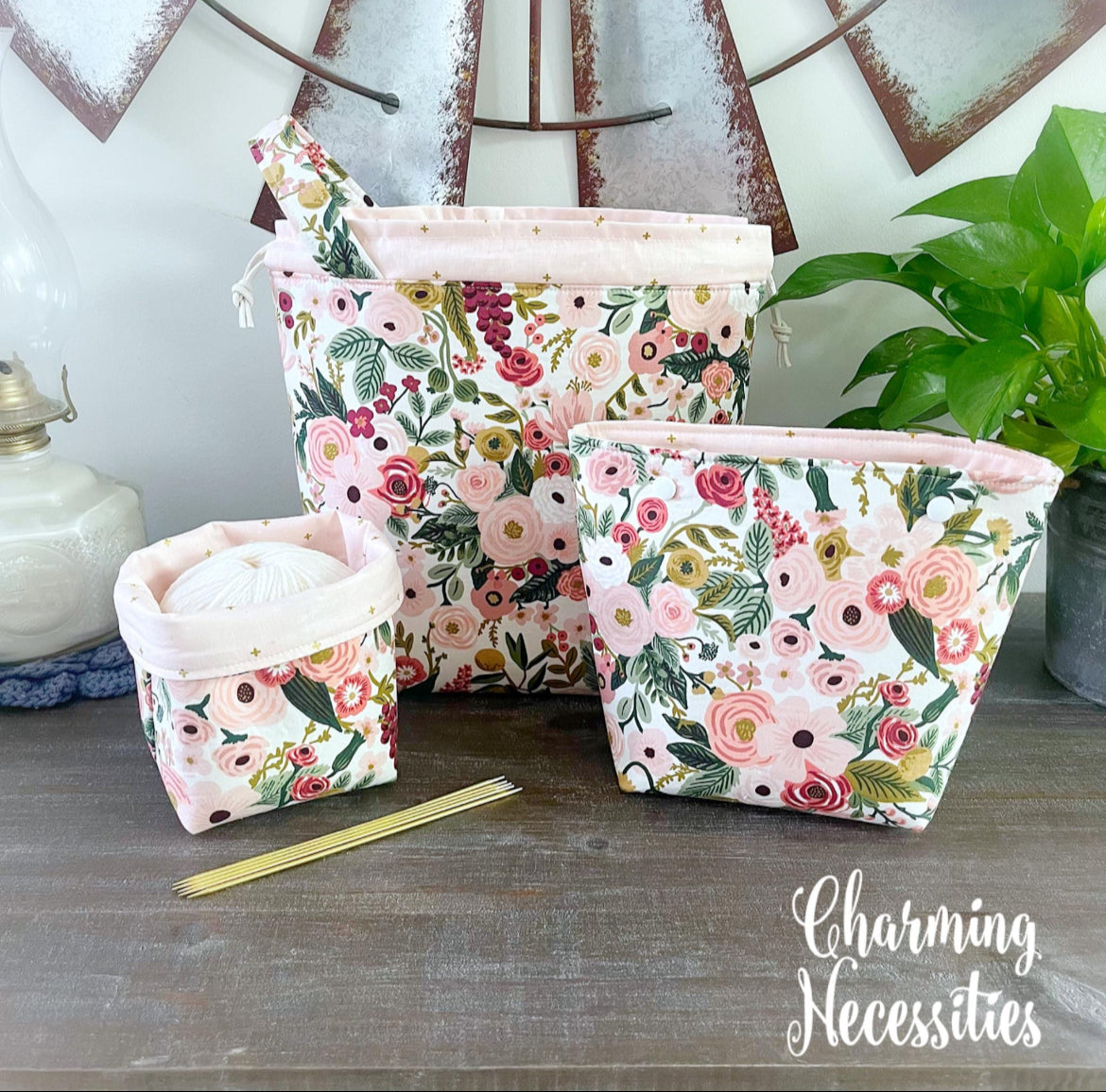 Set of floral fabric knitting bags on a wooden surface with 'Charming Necessities' branding.